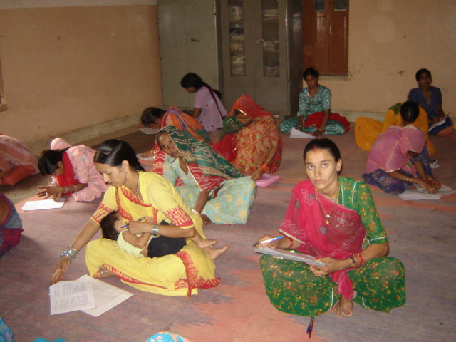 A woman writing while holding her child during a Meera Sansthan learning activity